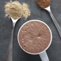 close-up  of maca latte with spoons of maca powder and cocoa powder next to it