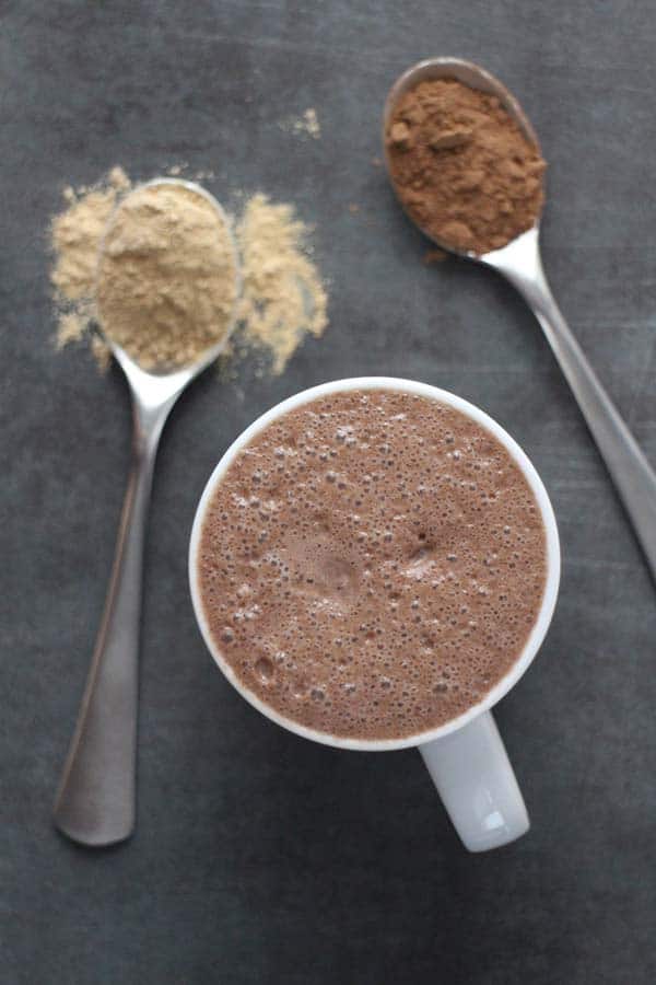 close-up  of maca latte with spoons of maca powder and cocoa powder next to it
