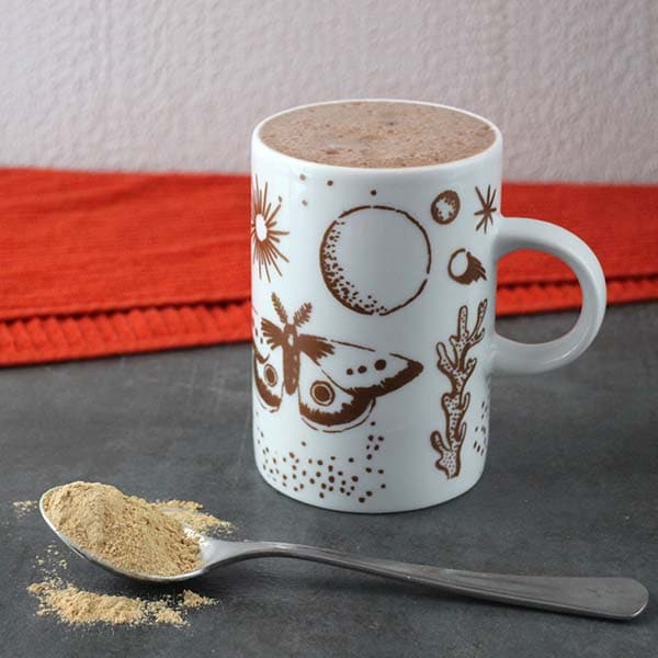 mug of maca latte next to a spoonful of maca powder