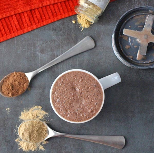 overhead photo of maca latte with spoons of maca powder and cocoa powder next to it