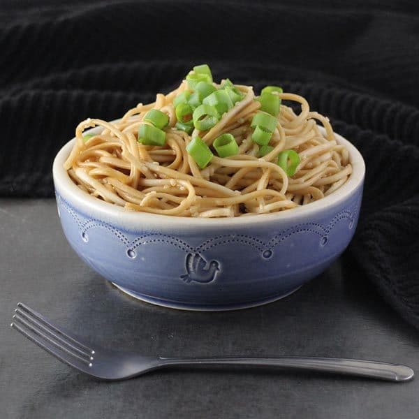 purple bowl of vegan sesame noodles on a gray table