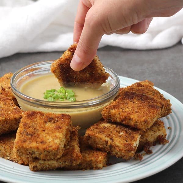 close-up of a hand dipping a vegan chicken nugget into "honey" mustard sauce