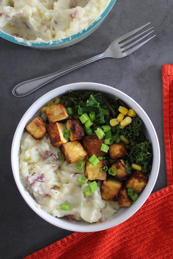 overhead photo of a vegan mashed potato bowl with tofu, kale, corn, and green onions