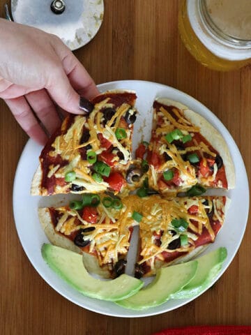 hand picking up a slice of vegan Mexican pizza with sliced avocado on the side