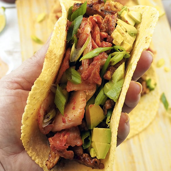 hand holding a corn tortilla stuffed with kimchi, soy curls, and avocado