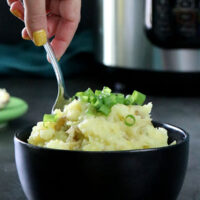 A person serving vegan colcannon from a bowl. Pressure cooker in the background
