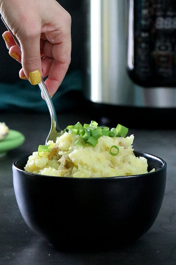 A person serving vegan colcannon from a bowl. Pressure cooker in the background