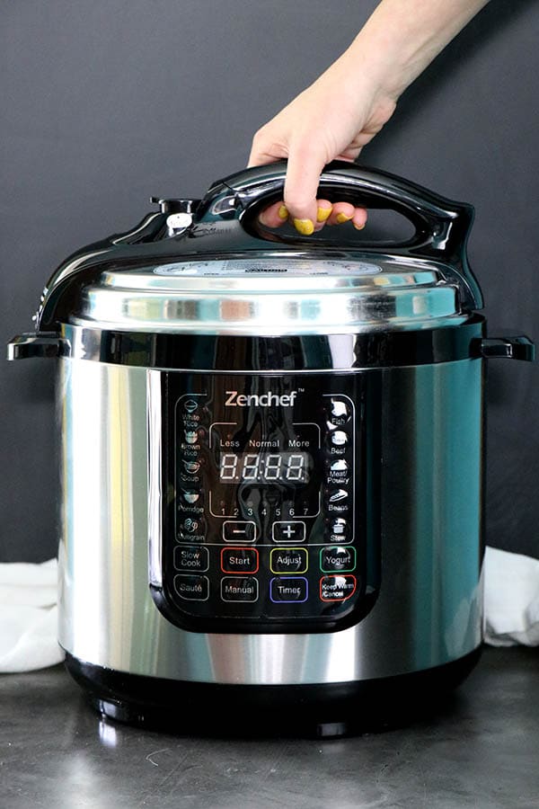 hand about to open an electric pressure cooker