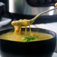 spoon lifting up a bite of vegan broccoli cheese soup with a pressure cooker in the background