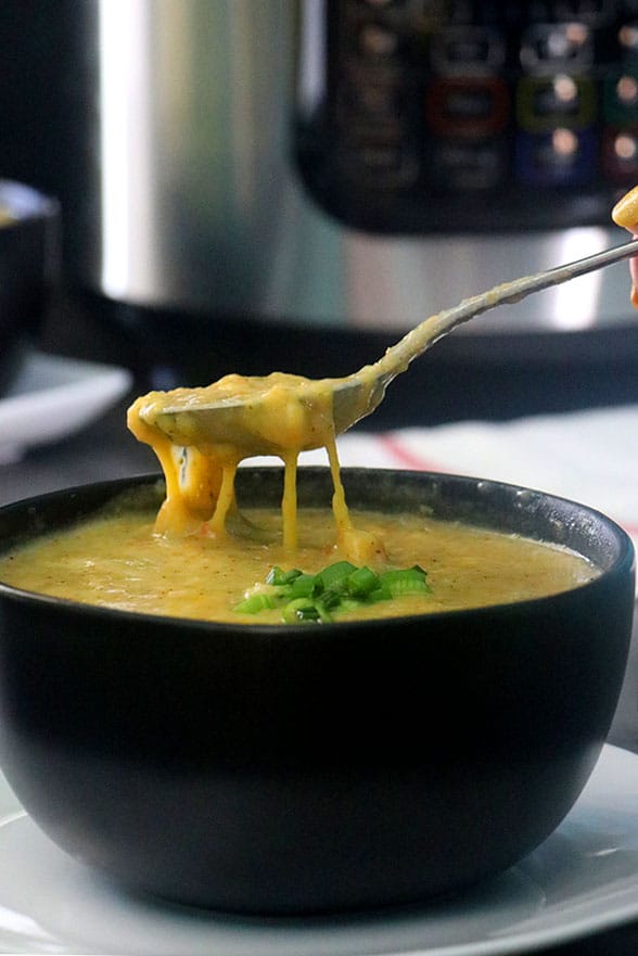 spoon lifting up a bite of vegan broccoli cheese soup with a pressure cooker in the background