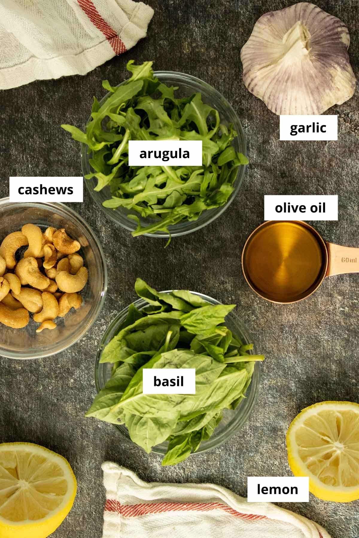 arugula pesto ingredients on a slate table, ingredients are labeled with text