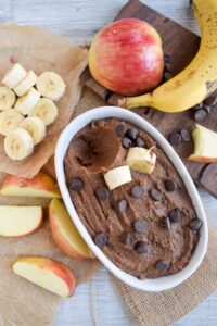 overhead photo of vegan chocoalte peanut butter hummus in a serving bowl next to apples and bananas
