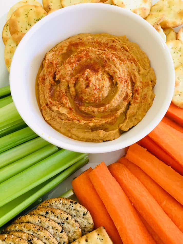 close-up of peanut butter hummus in the middle of a veggie tray with celery sticks, carrots, and crackers
