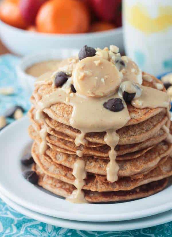photo of a stack of vegan peanut butter pancakes topped with peanut butter syrup, sliced bananas, and chocolate chips