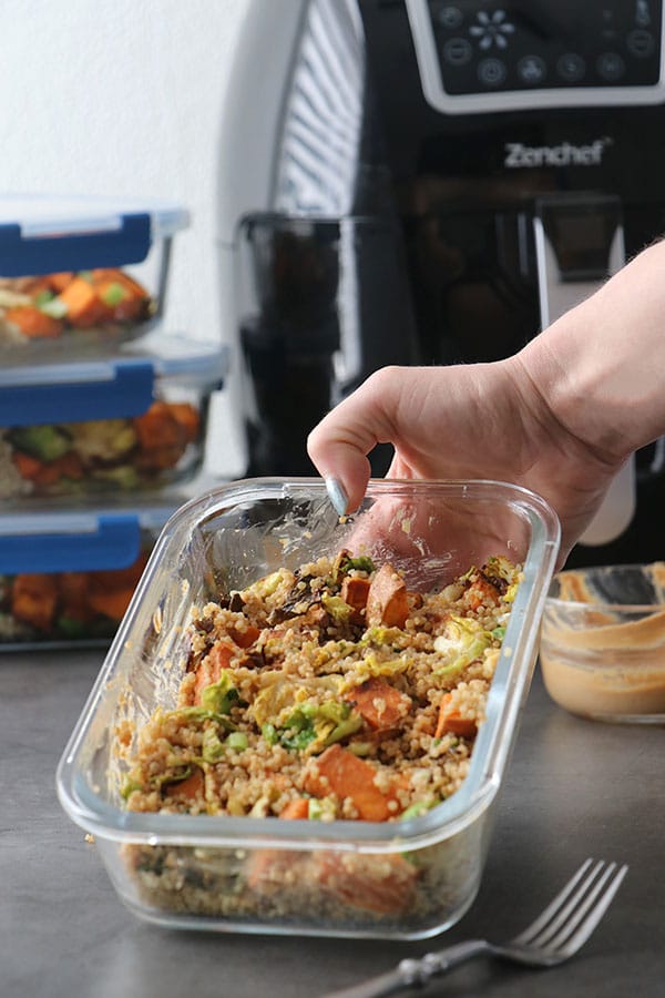Hand setting down a sweet potato meal prep container with sauce mixed in