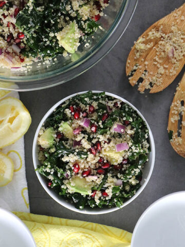 a bowl filled with superfood quinoa salad with kale, red onion, avocado, and pomegranate seeds.