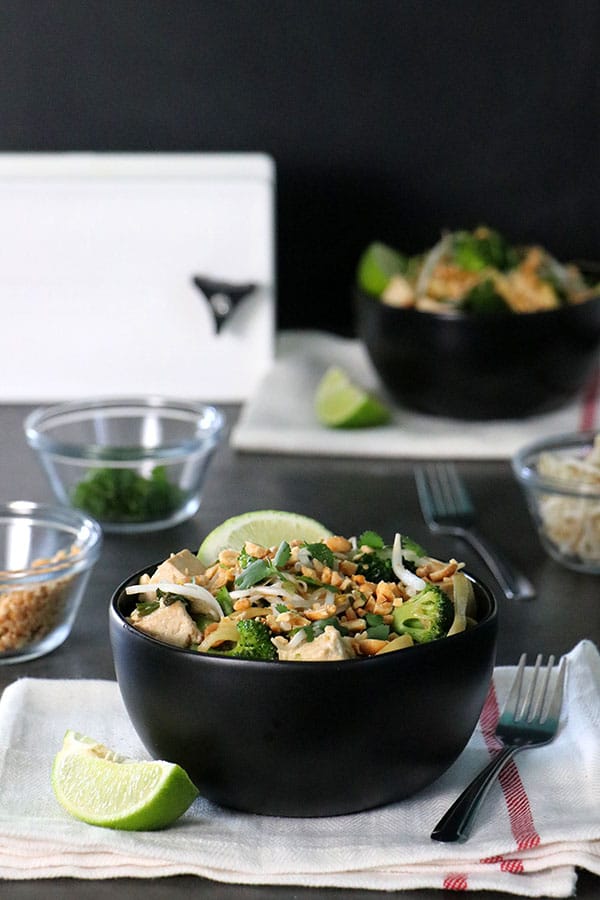 bowl of tofu with noodles with small bowls of toppings scattered on the table