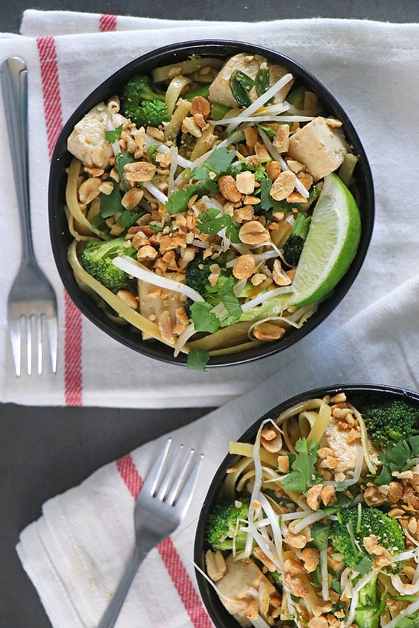 overhead photograph of tofu with noodles and broccoli in black bowls on ivory tea towels