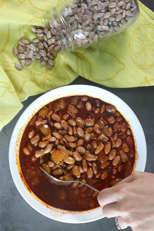 smoky pinto beans in a white bowl next to a yellow tea towel and dried beans