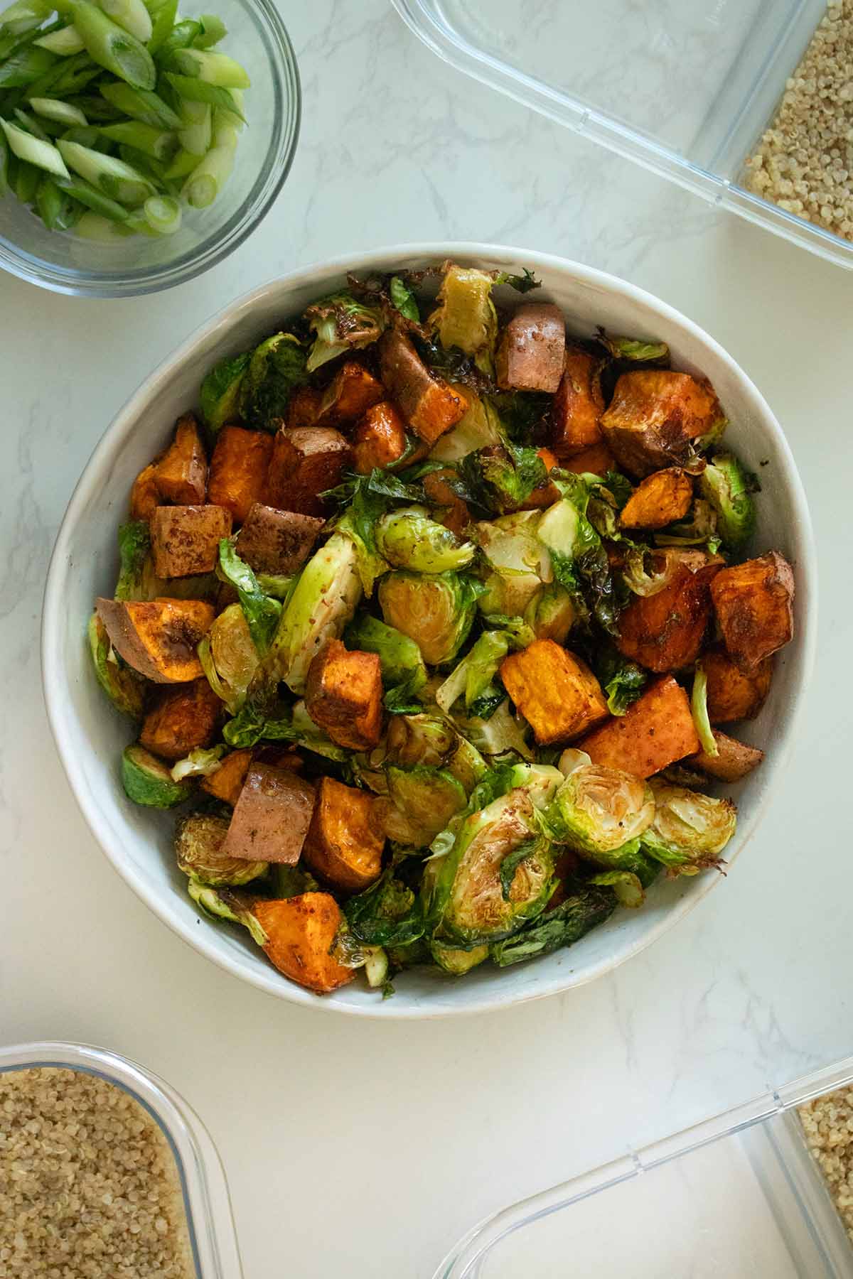 air fryer Brussels sprouts and sweet potatoes in a bowl surrounded by meal prep containers