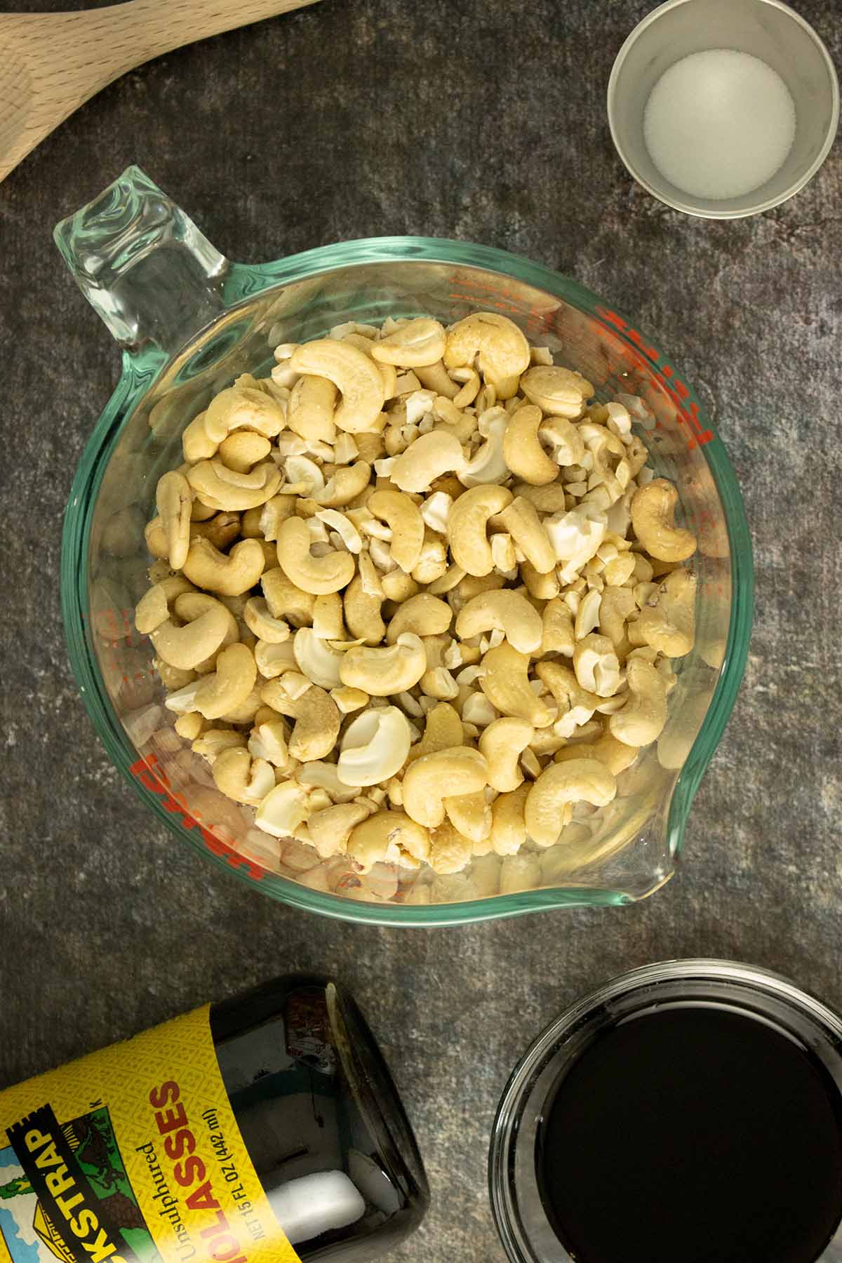 raw cashews on a table with containers of molasses, liquid smoke, and salt