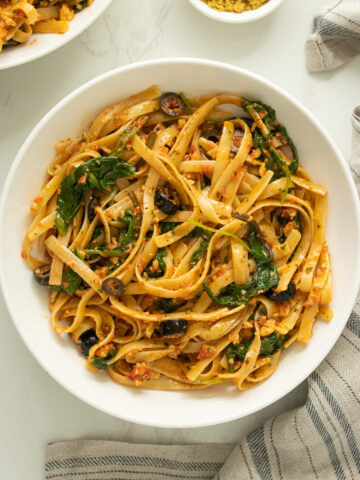 bowl of red pepper pesto pasta with spinach and black olives