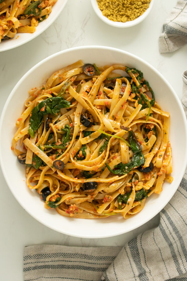 bowl of red pepper pesto pasta with spinach and black olives