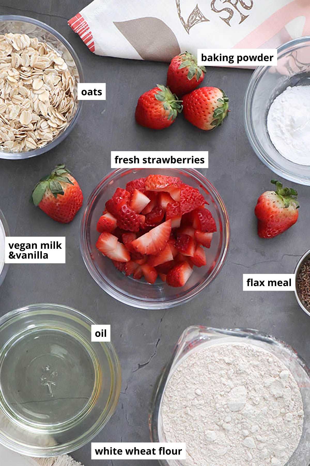 oats, strawberries, and other muffin ingredients in bowls on a slate table
