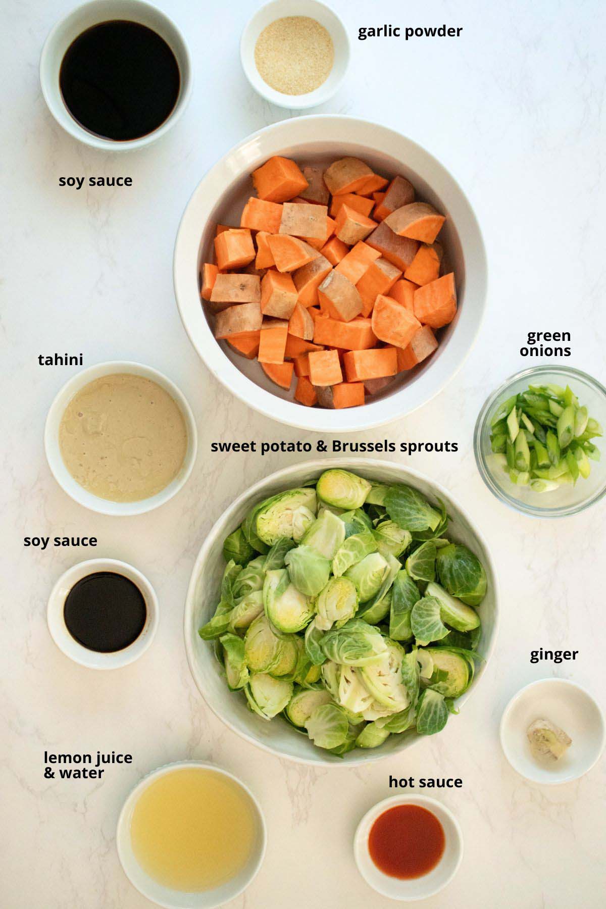 sweet potatoes, Brussels sprouts, and other meal prep ingredients in bowls on a white table