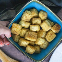 hand placing a bowl of crispy baked tofu onto a wooden table
