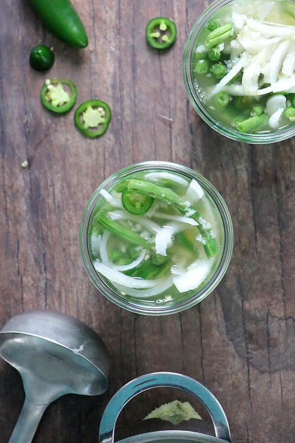 green bean pickles in glass jars with jalapenos and a ladle on the table