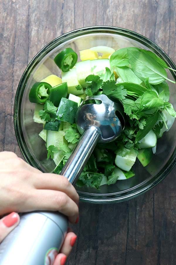 using your immersion blender on a bowl of cucumber, pineapple, herbs, and jalapeno