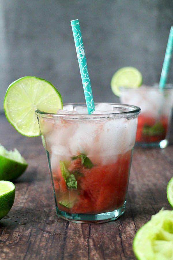 photo of a tequila watermelon smash cocktail in a glass on a wooden table with limes