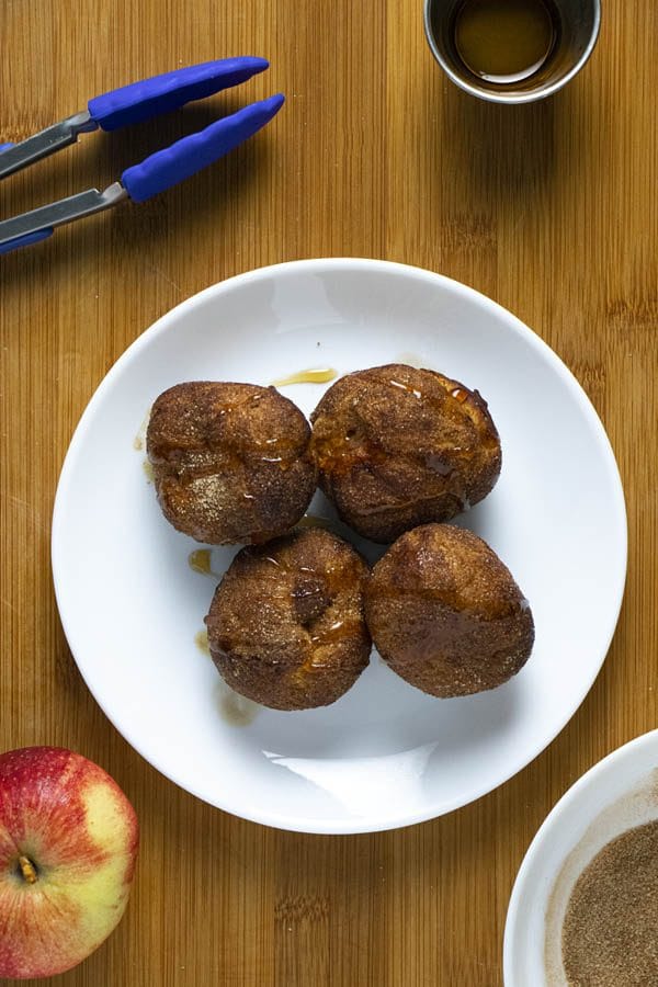 overhead photo of air fryer apple fritters on a plate with ingredients and tongs on the table