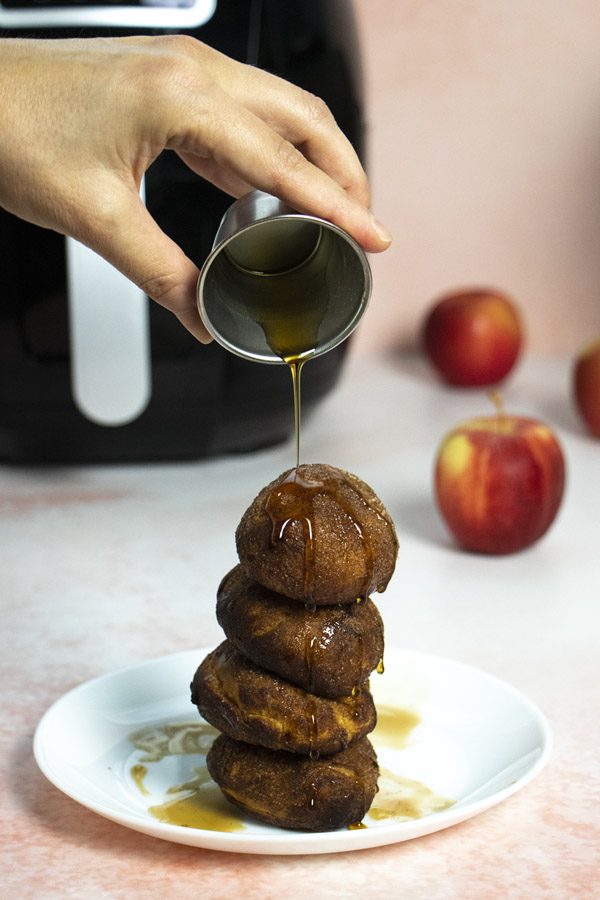 pouring maple syrup onto a stack of air fryer apple fritters