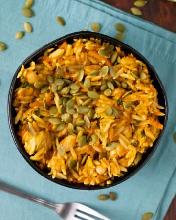 bowl of vegan orzo in pumpkin sauce topped with pumpkin seeds