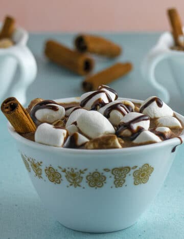 vegan hot chocolate in a mug with a cinnamon stick, marshmallows, and chocolate syrup