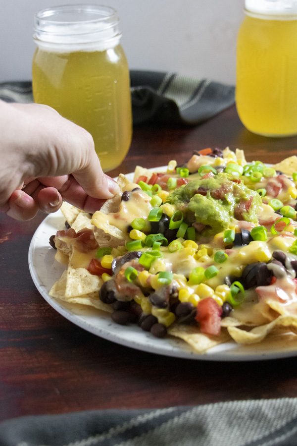 hand grabbing a chip from a plate of vegan nachos