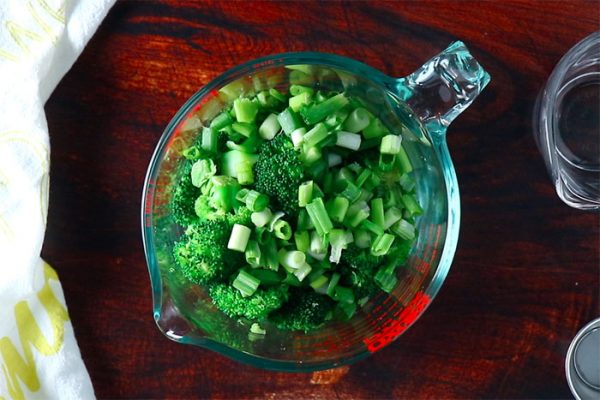 cooked broccoli mixed with green onions in a glass measuring bowl