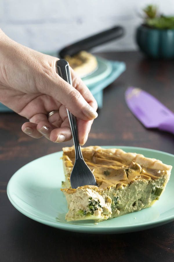 using a fork to take a bite from a slice of vegan quiche with broccoli