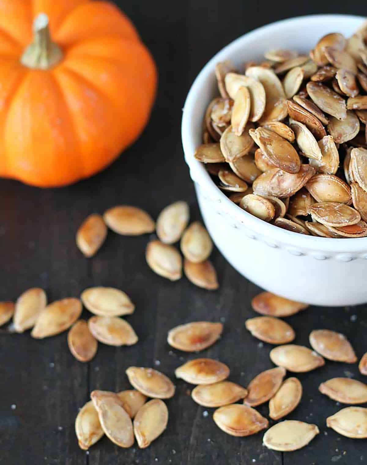 roasted winter squash seeds in a bowl next to a miniature pumpkin