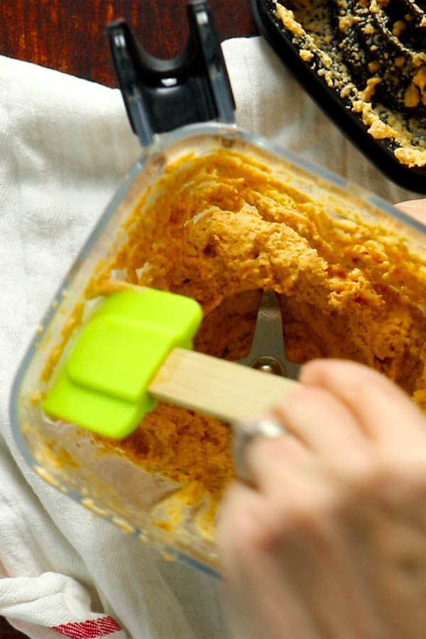 hand using a rubber spatula to scrape down the sides of the blender