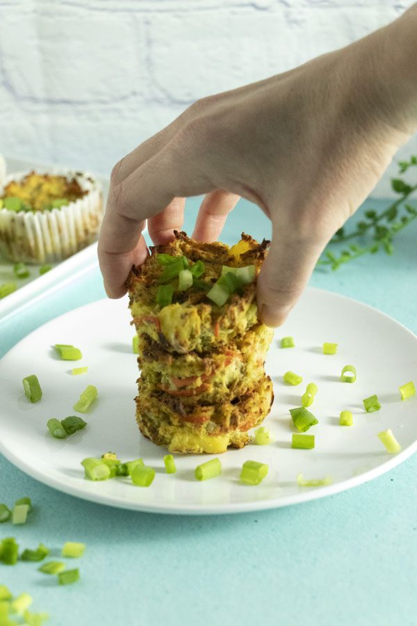 stack of vegan potato cakes on a plate with green onion pieces and a hand placing one more on top of the stack