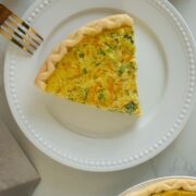 overhead shot of a slice of vegan quiche on a plate next to the pan of quiche
