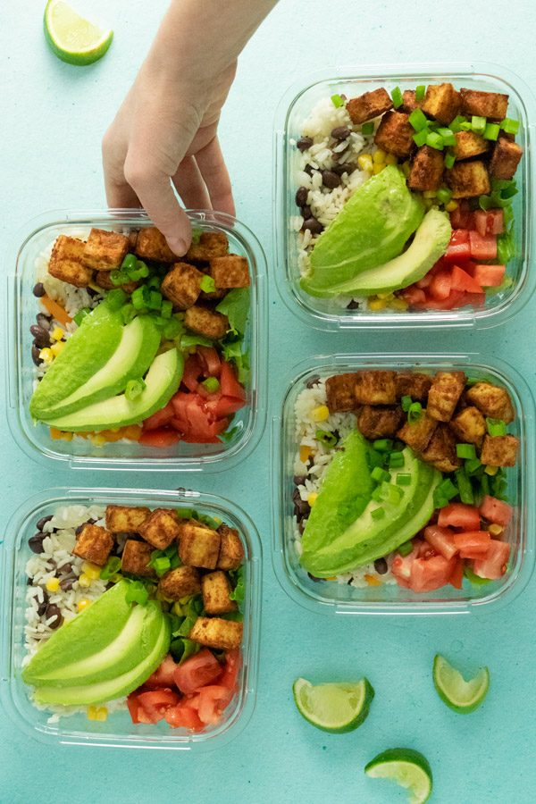 4 meal prep containers on a table with beans and rice, tofu, and toppings