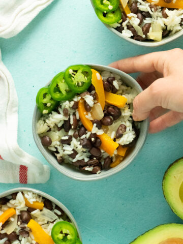 hand serving a bowl of vegan black beans and rice with bell peppers and sliced jalapeno