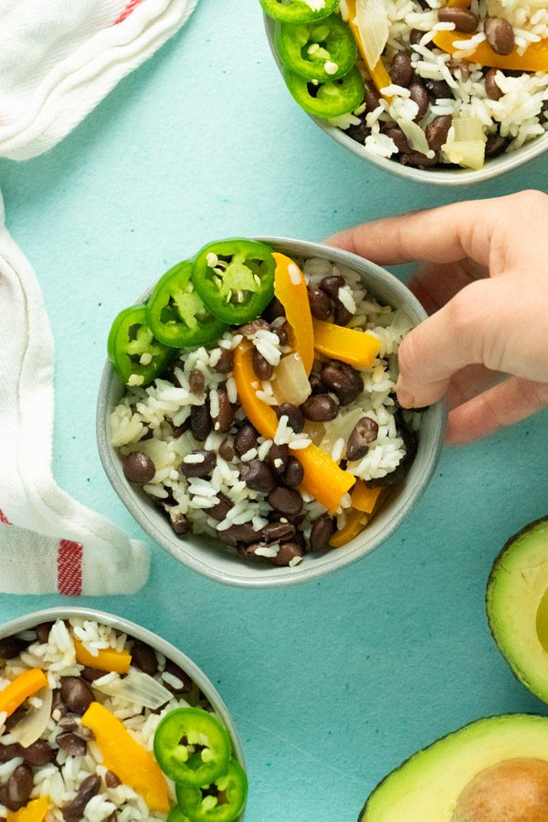 hand serving a bowl of vegan black beans and rice with bell peppers and sliced jalapeno