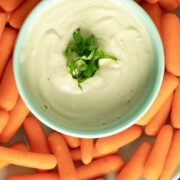 overhead photo of garlic cashew cream in a blue bowl surrounded by baby carrots