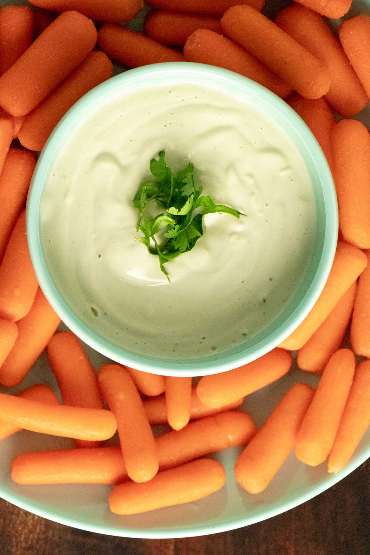 overhead photo of garlic cashew cream in a blue bowl surrounded by baby carrots