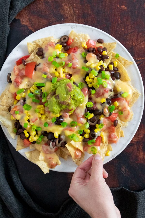 hand taking a chip from a plate of fully loaded vegan nachos